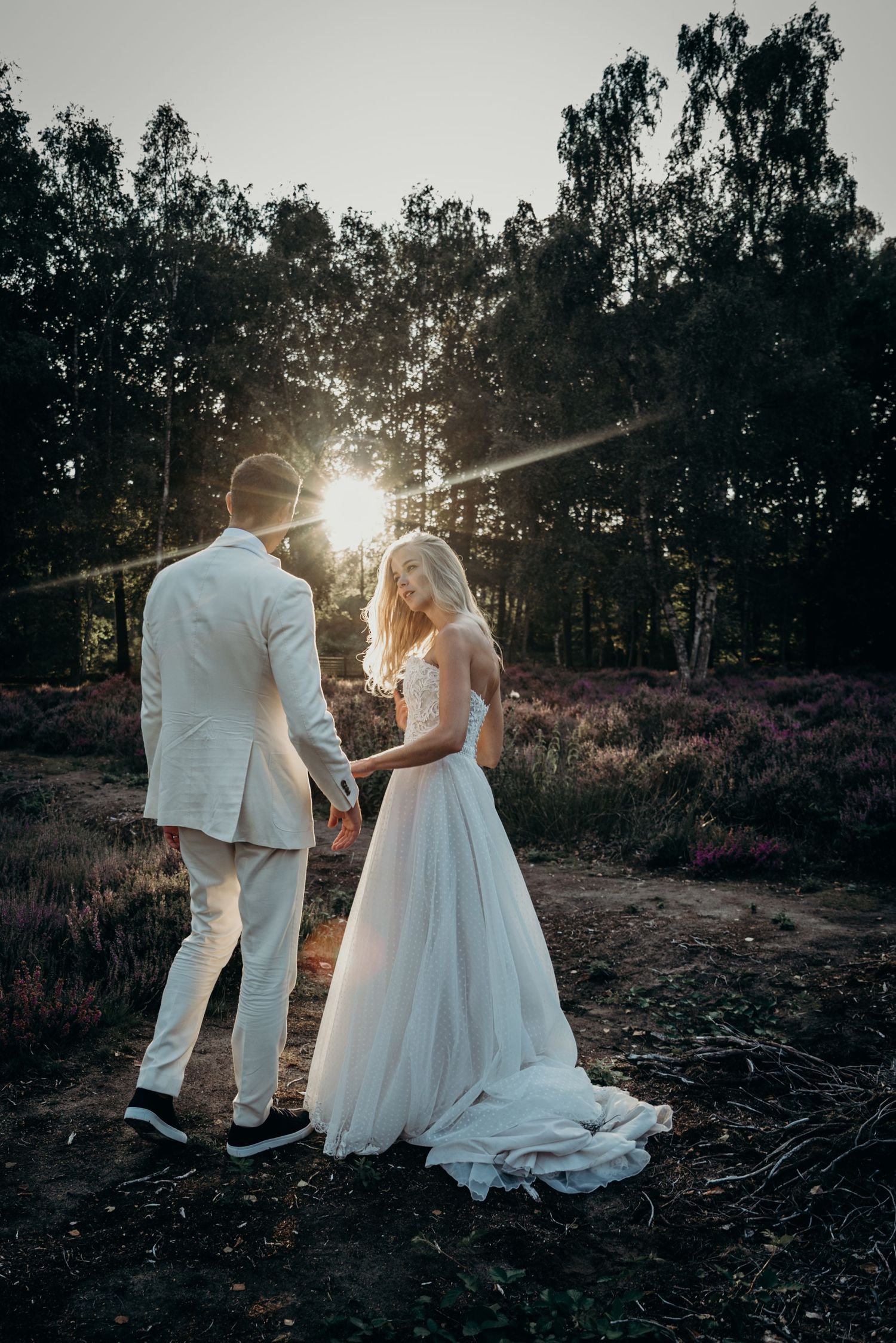 Backlit wedding couple stands together in golden sunlight among trees.