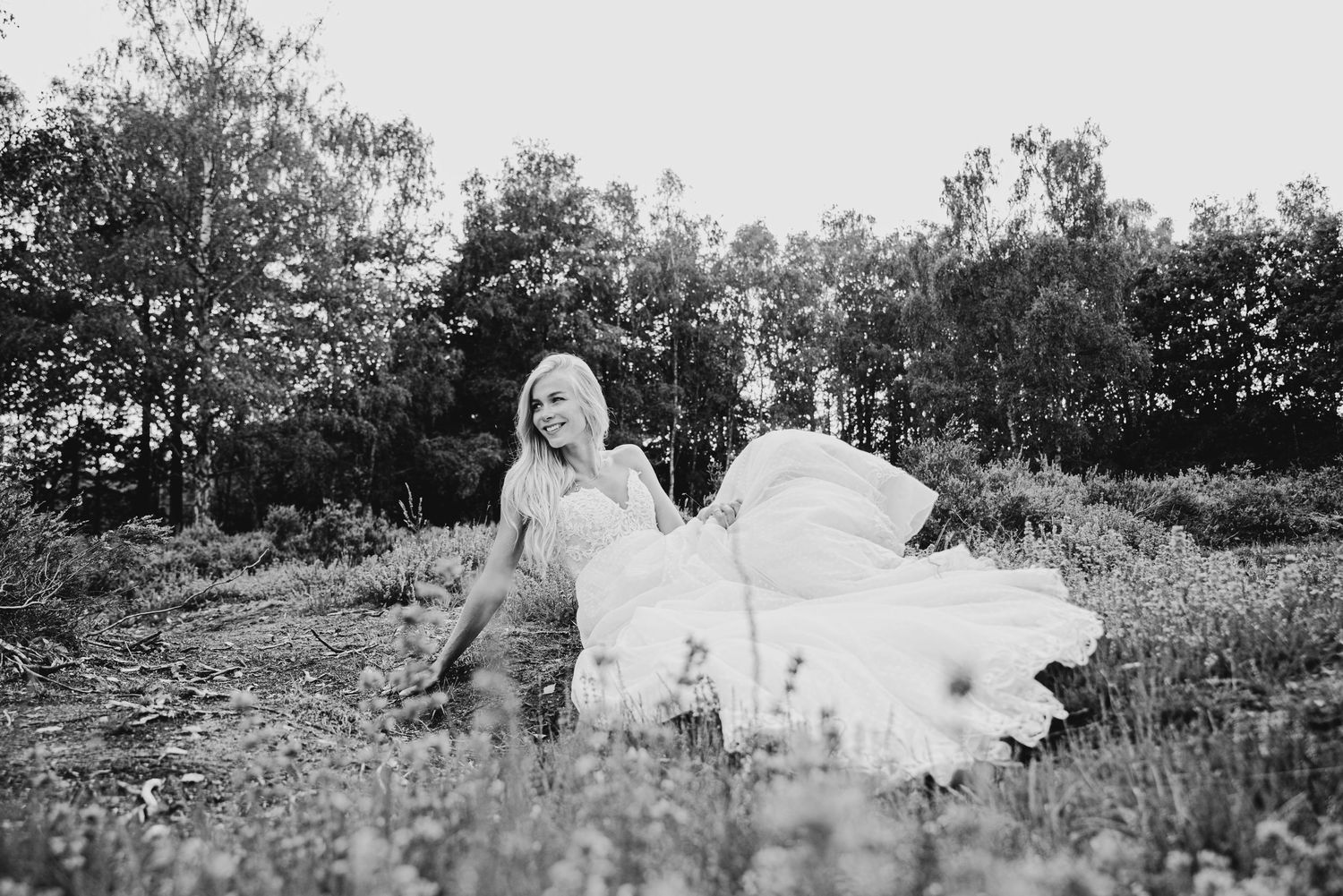 Black and white photo of a bride in flowing dress walking through a meadow.