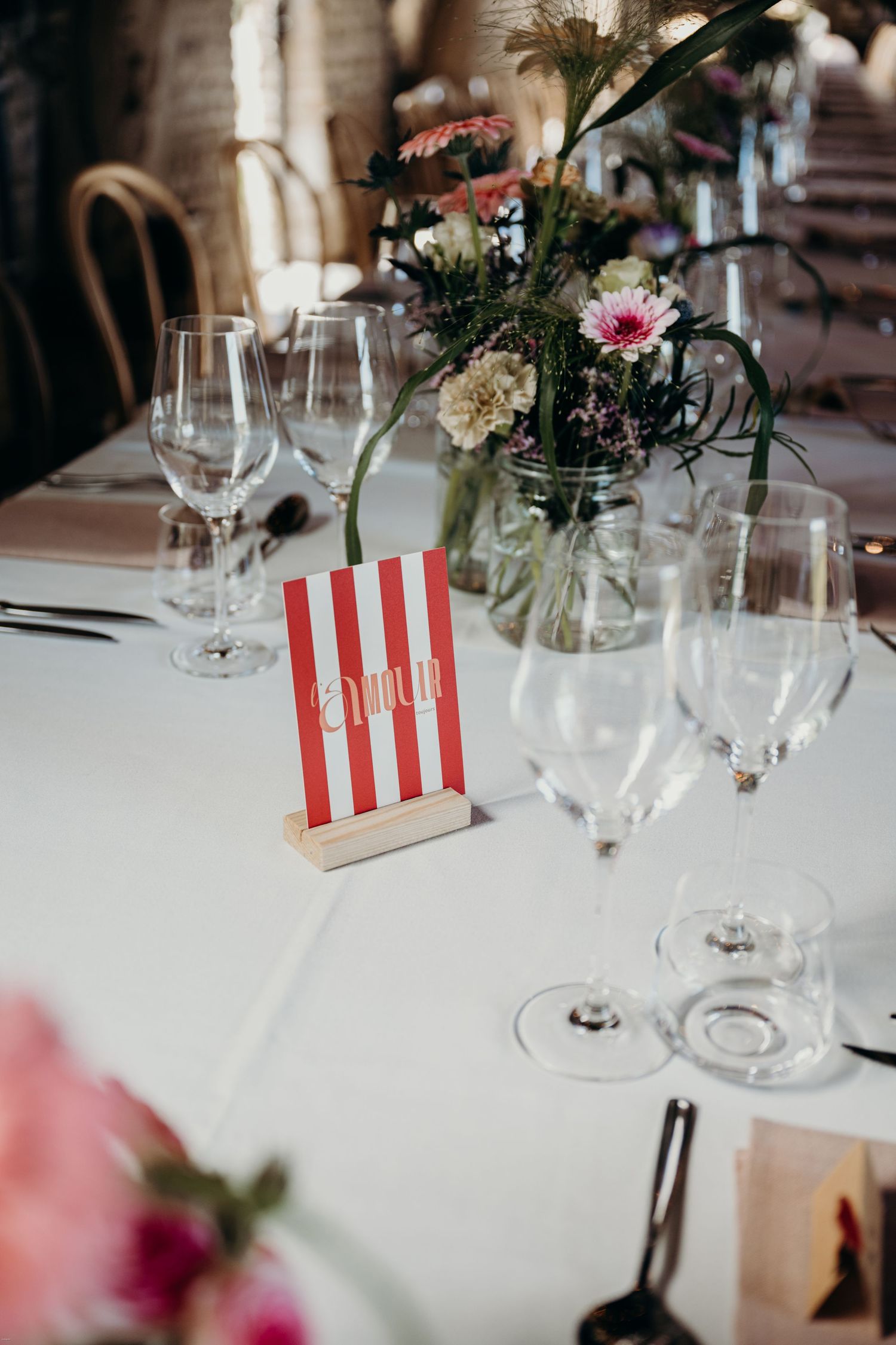 Elegant table setting with wine glasses, floral centerpiece and red striped table number.