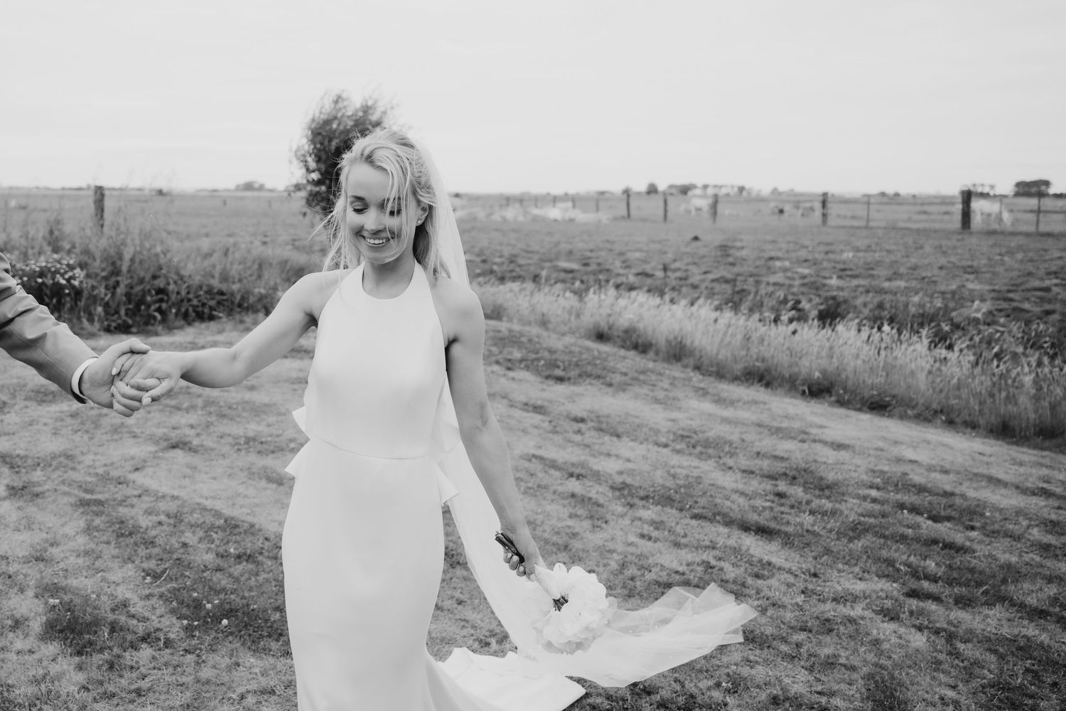 White wedding dress and veil billowing dramatically in the breeze on a grassy hill.
