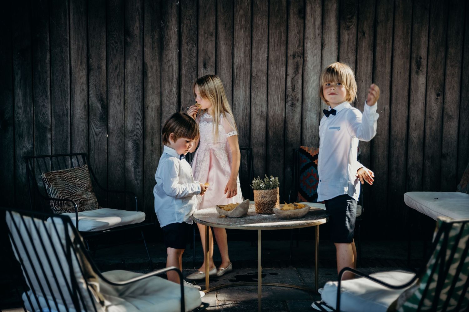Playful wedding party scene around a small table with rustic wooden backdrop.