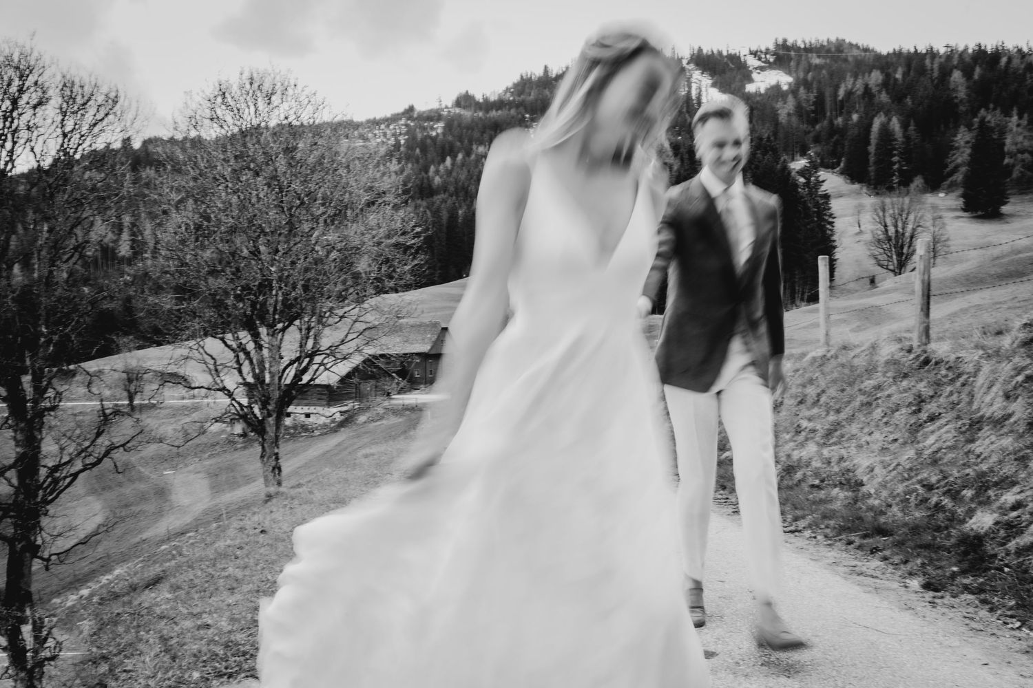 Bride in flowing white dress walks through scenic mountain landscape.
