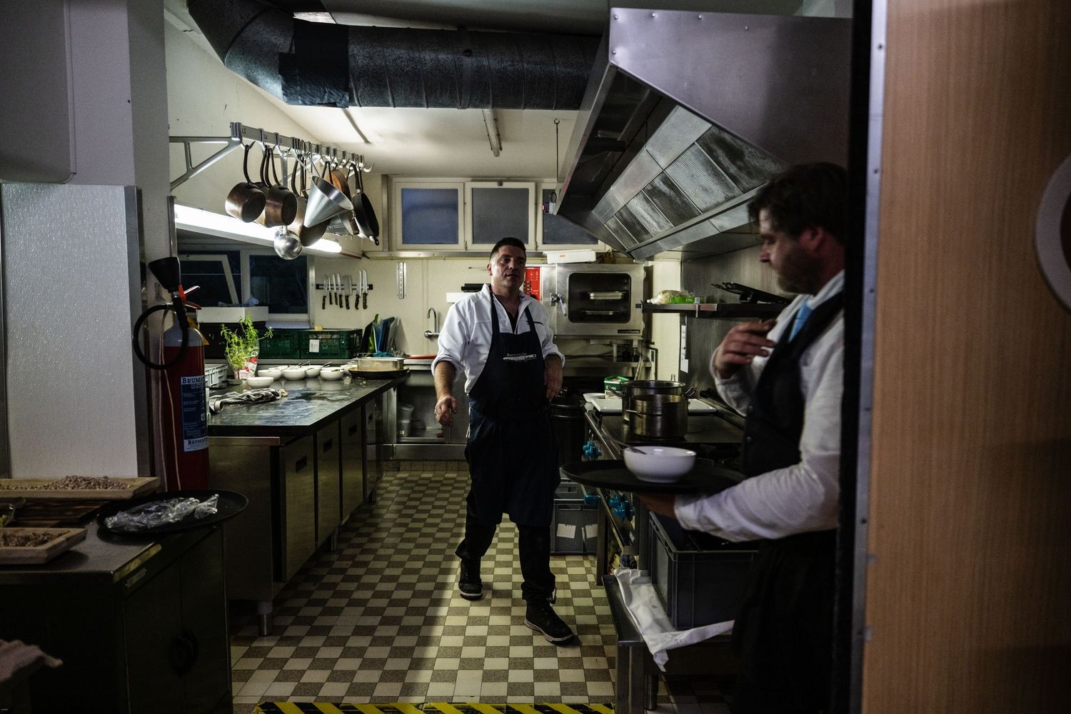 Interior sequence showing a dimly lit industrial kitchen or workspace with tiled floors.