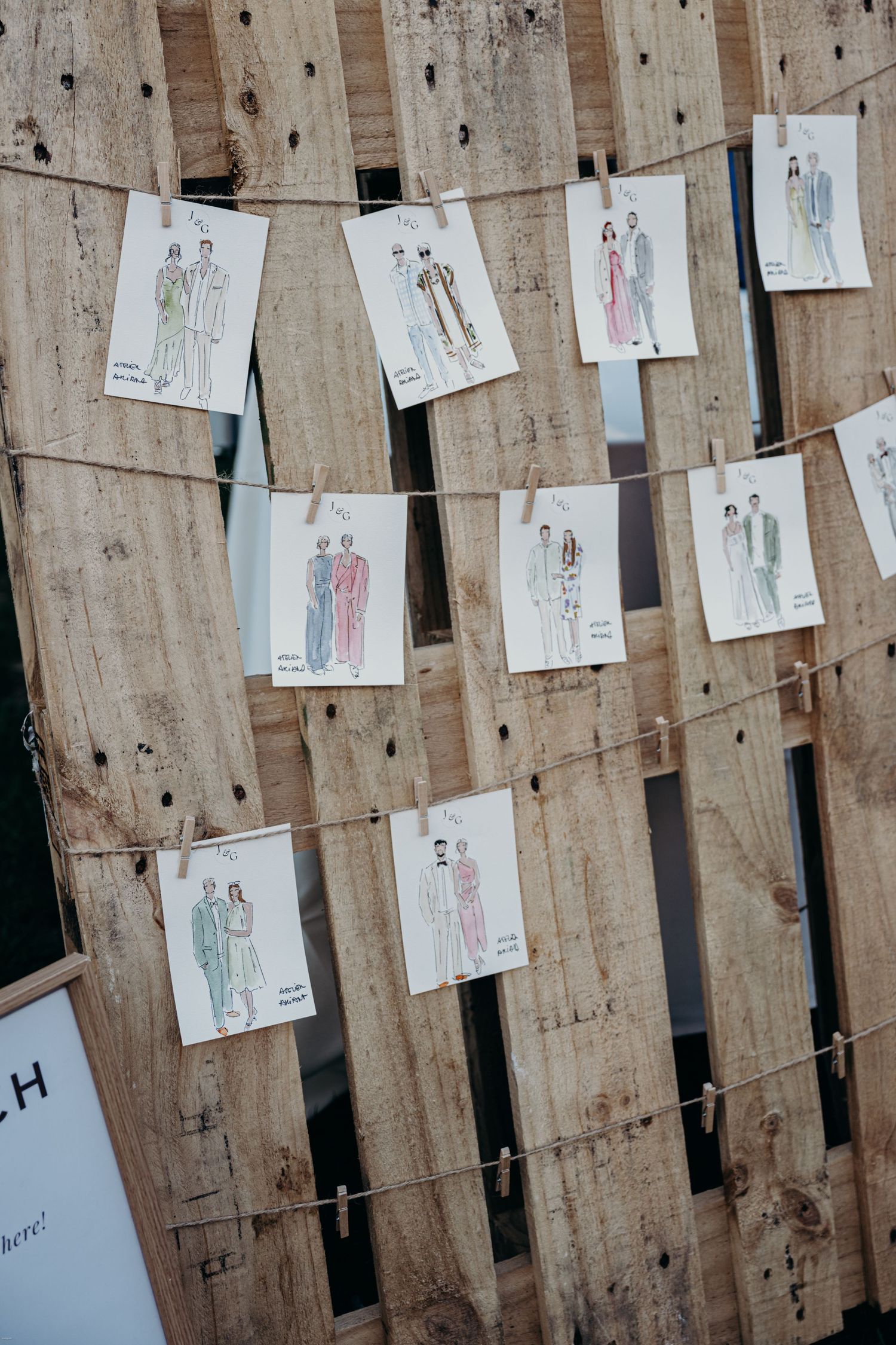 Hand-drawn fashion illustrations displayed on wooden boards at a wedding event.