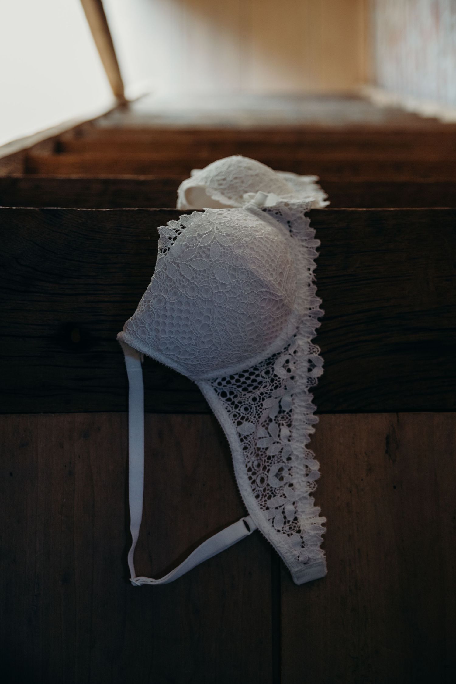 Delicate white lace bonnet with intricate floral patterns hangs on a dark wooden beam in vintage style.