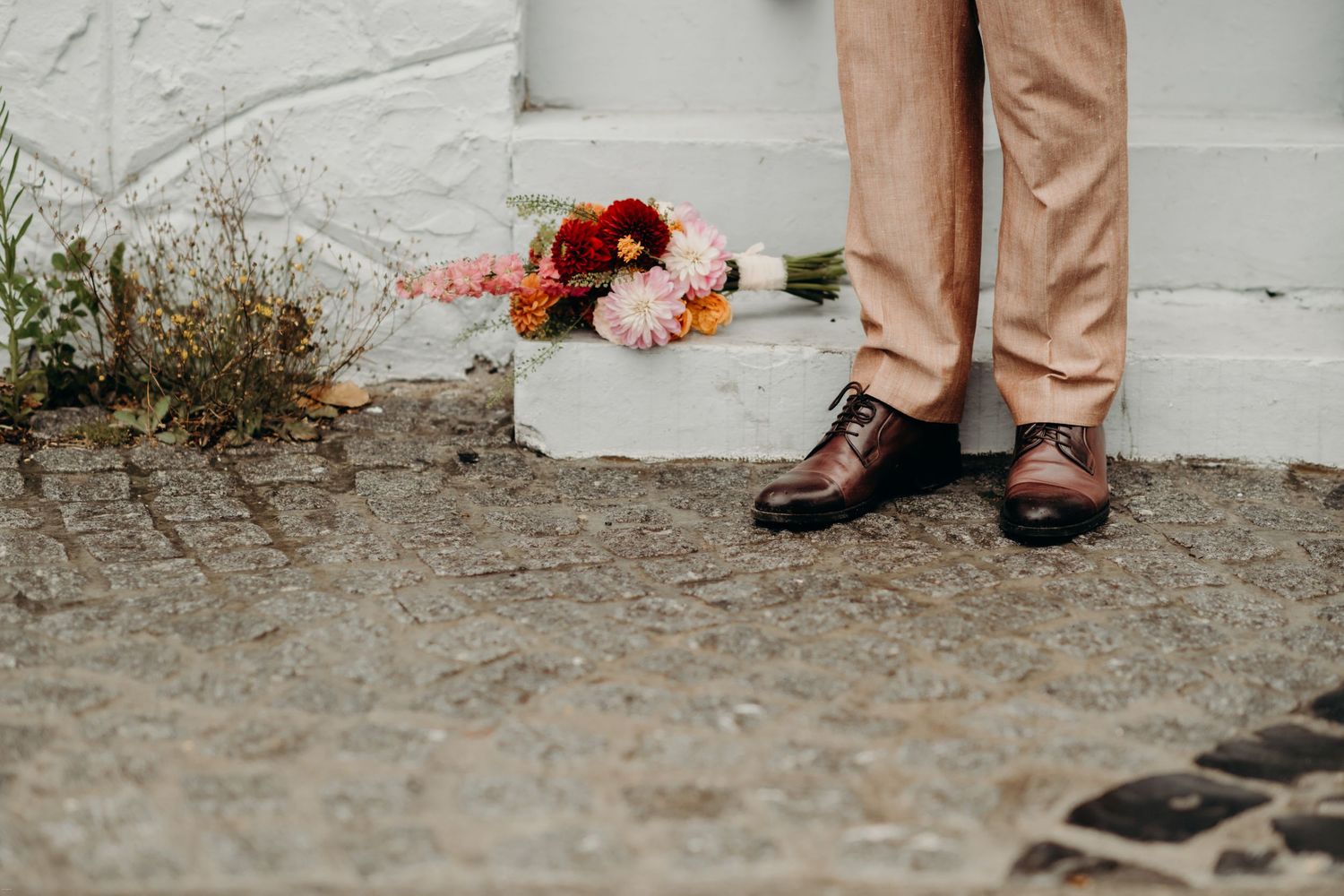 Detail shot of formal shoes and attire against a white wall.