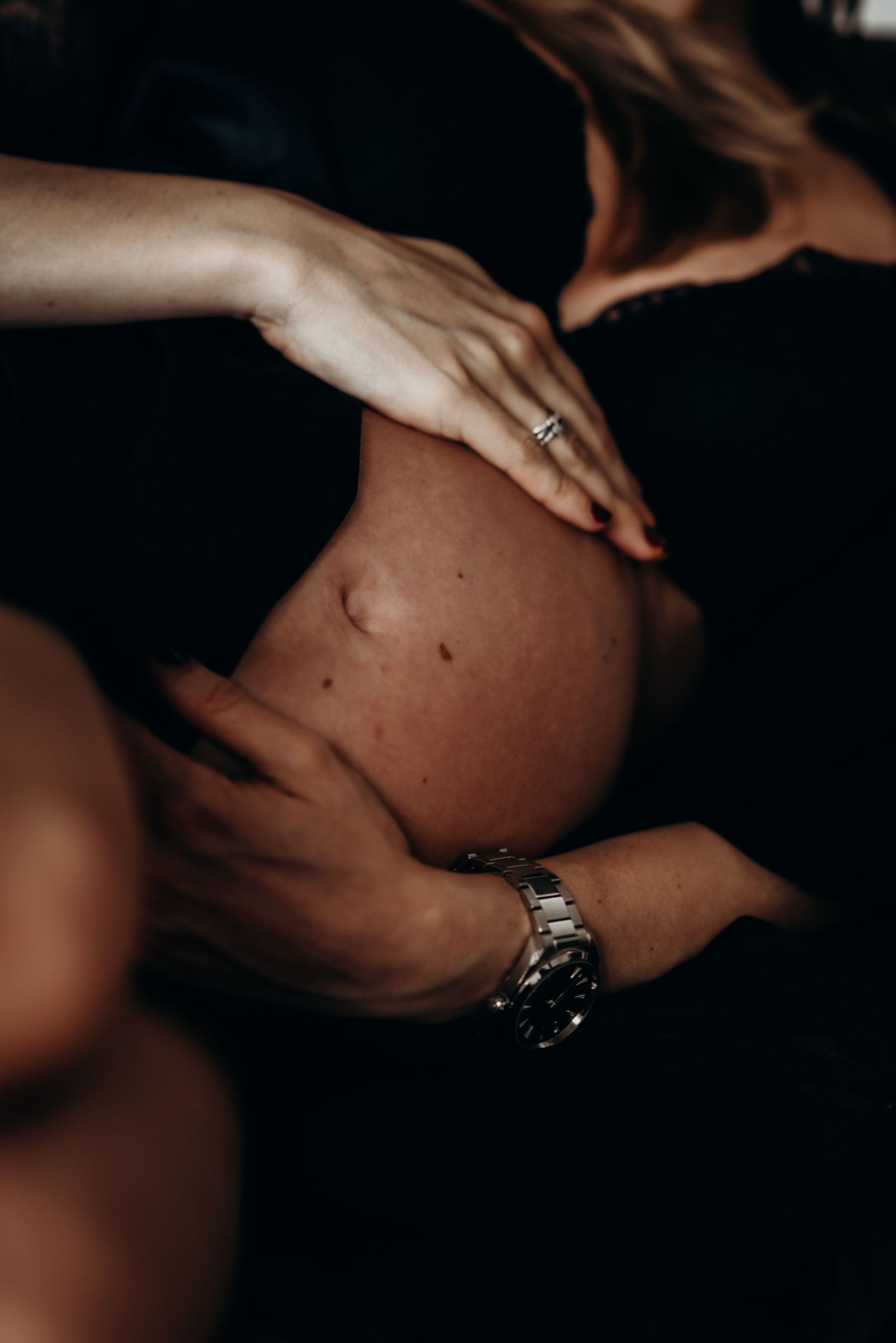 Artistic series of maternity photos showing a pregnant belly in moody lighting with hands and jewelry details.