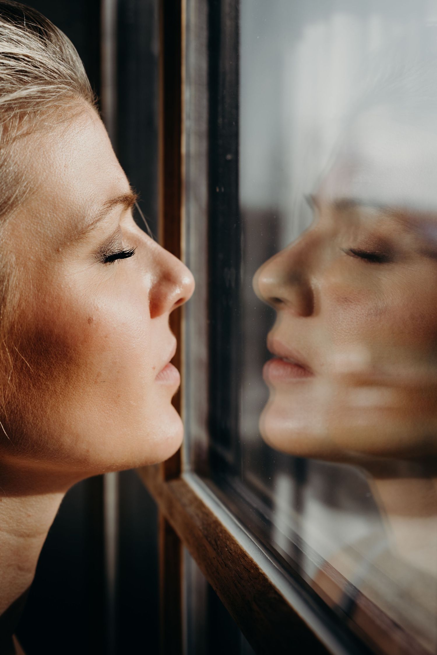 Close-up profile view of someone leaning against a window pane with their reflection visible in the glass.