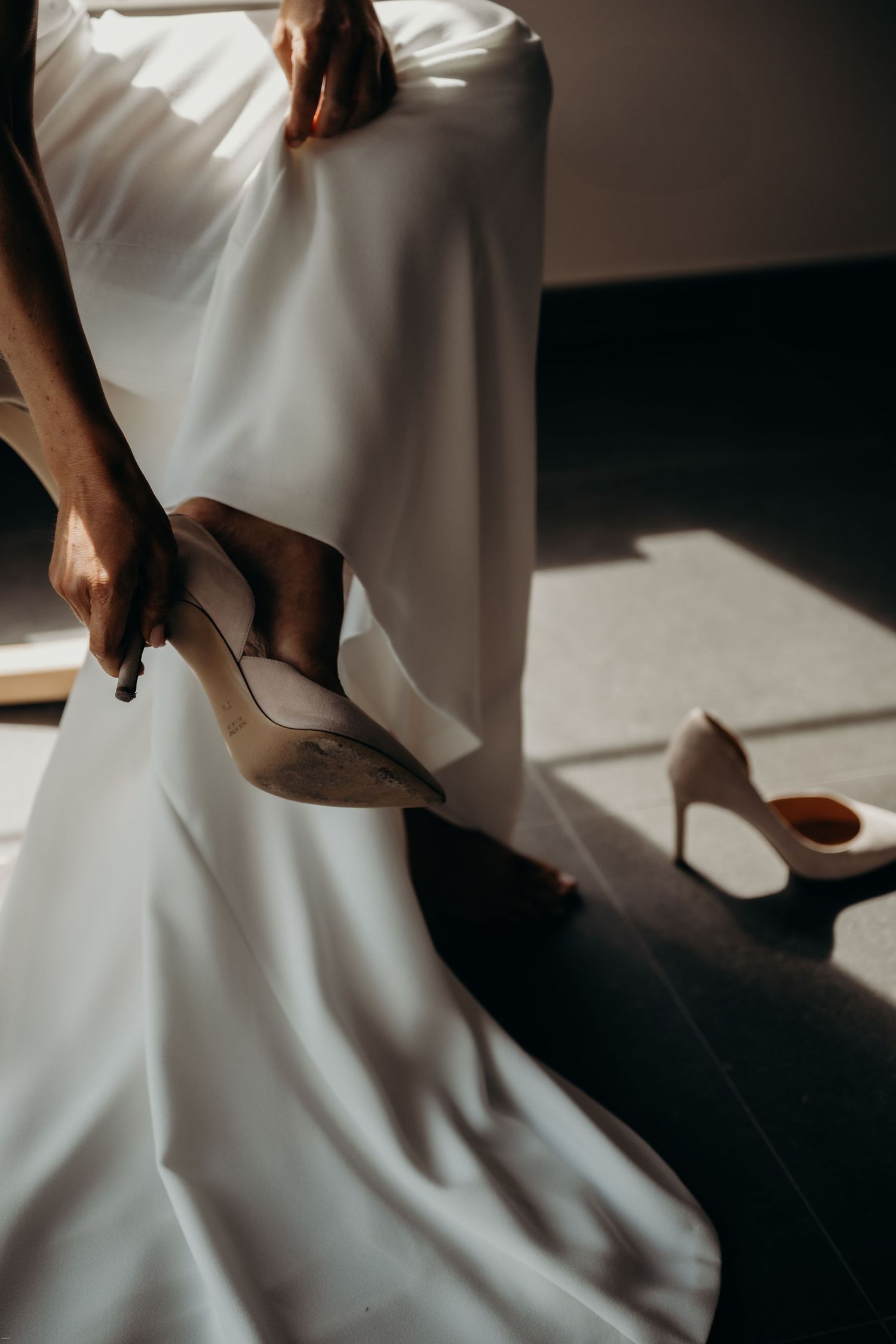 Artistic close-up shots of a white wedding dress and shoes in dramatic lighting.