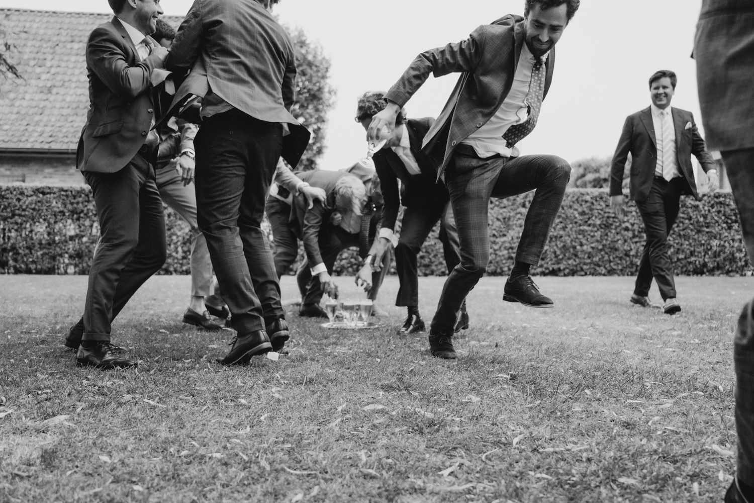 Black and white photo of wedding guests dancing energetically outdoors.