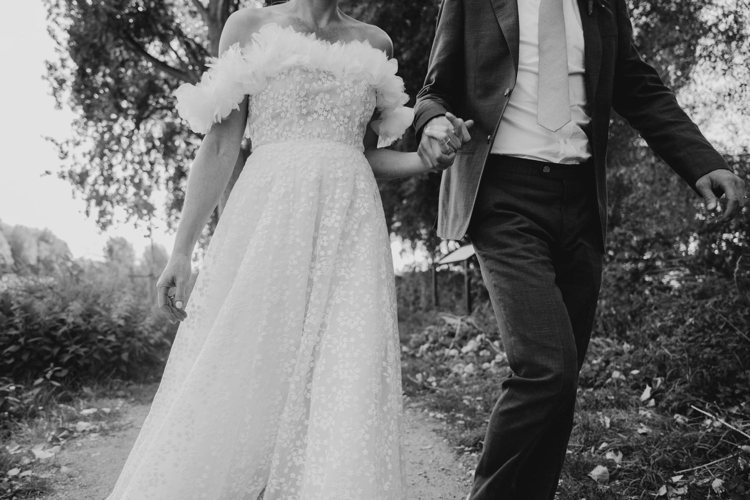 Black and white photo of a couple in wedding attire holding hands outdoors.