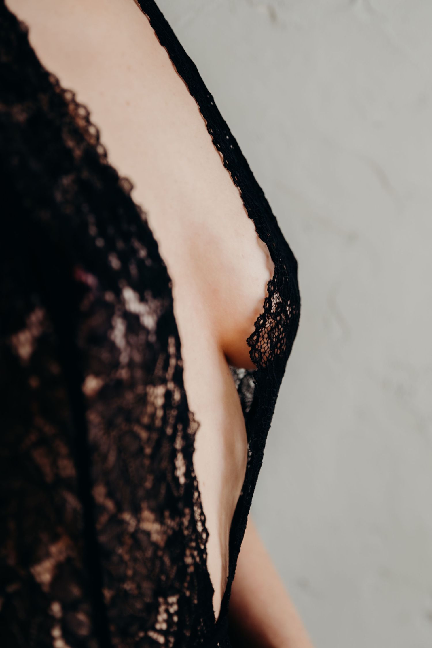 Close-up detail of black lace fabric against pale skin creating a sensual contrast against a light background.