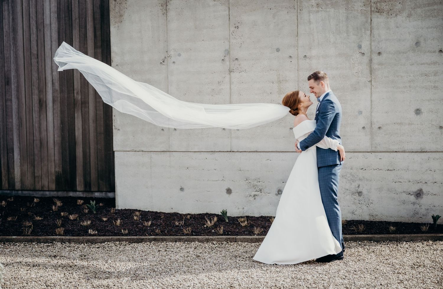 Panoramic shot of newlyweds dancing against concrete wall with flowing white wedding dress.