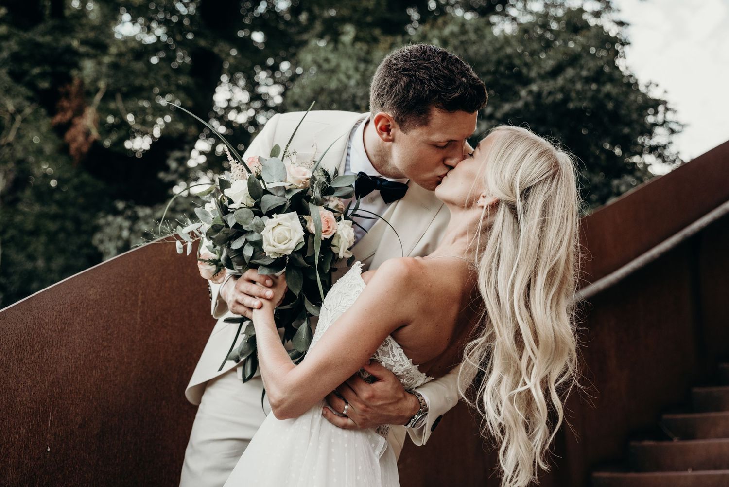 A romantic wedding portrait of a couple embracing on stairs with a floral bouquet.