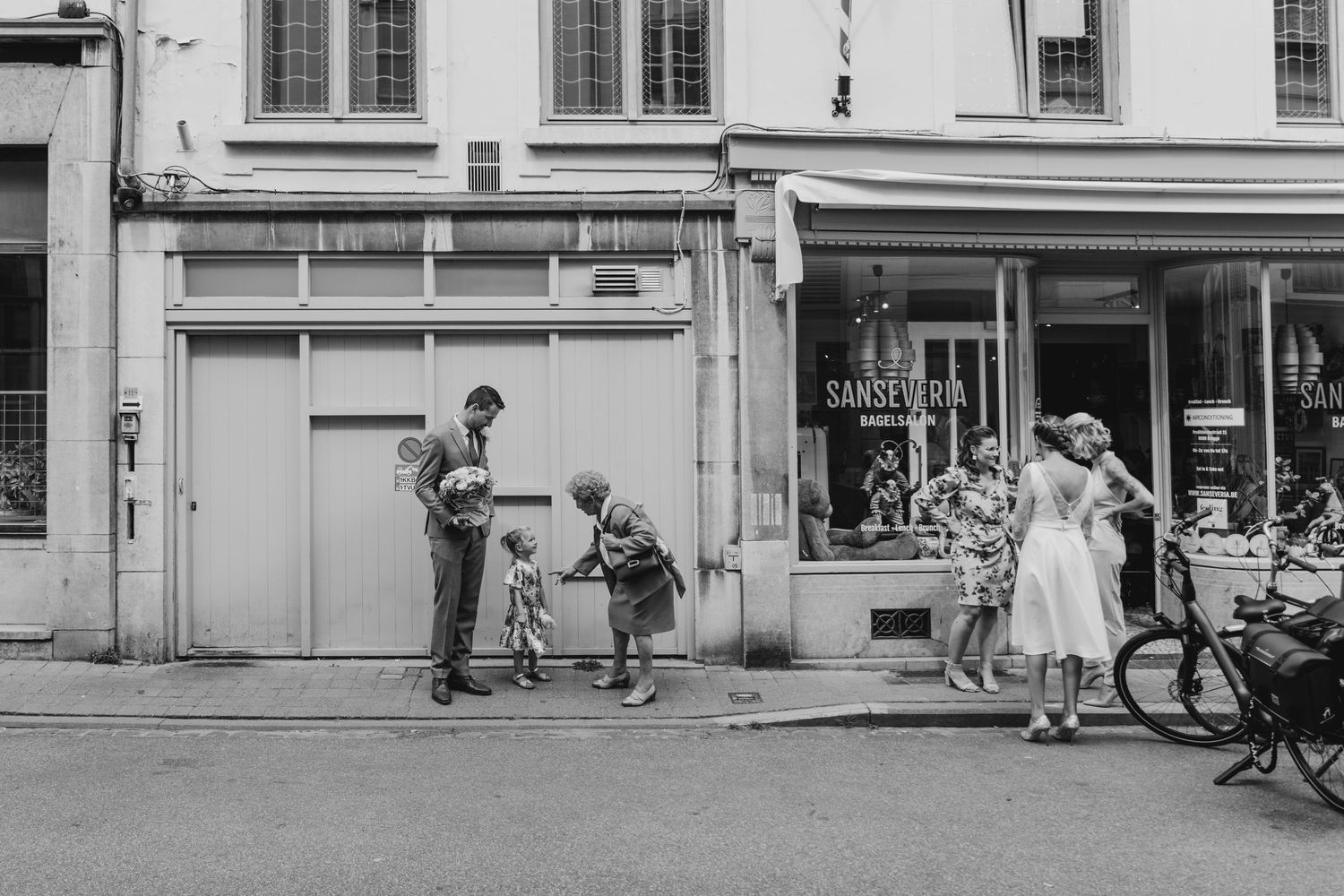 Vintage black and white street scene showing storefronts and pedestrians.