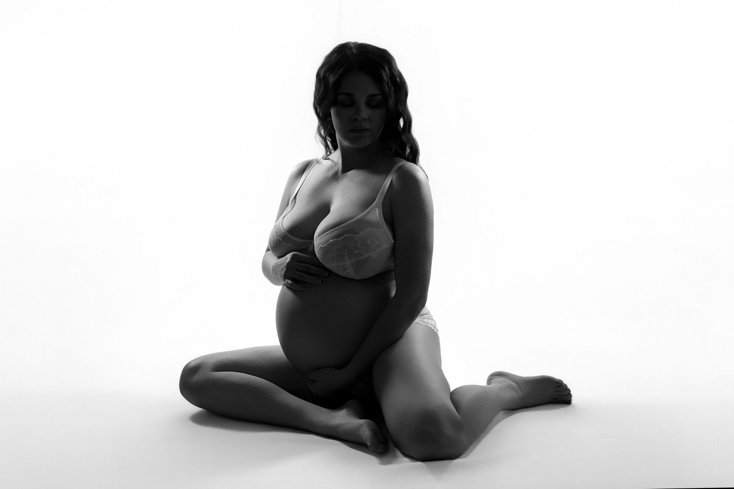 A woman posing for a maternity boudoir session against a white background.