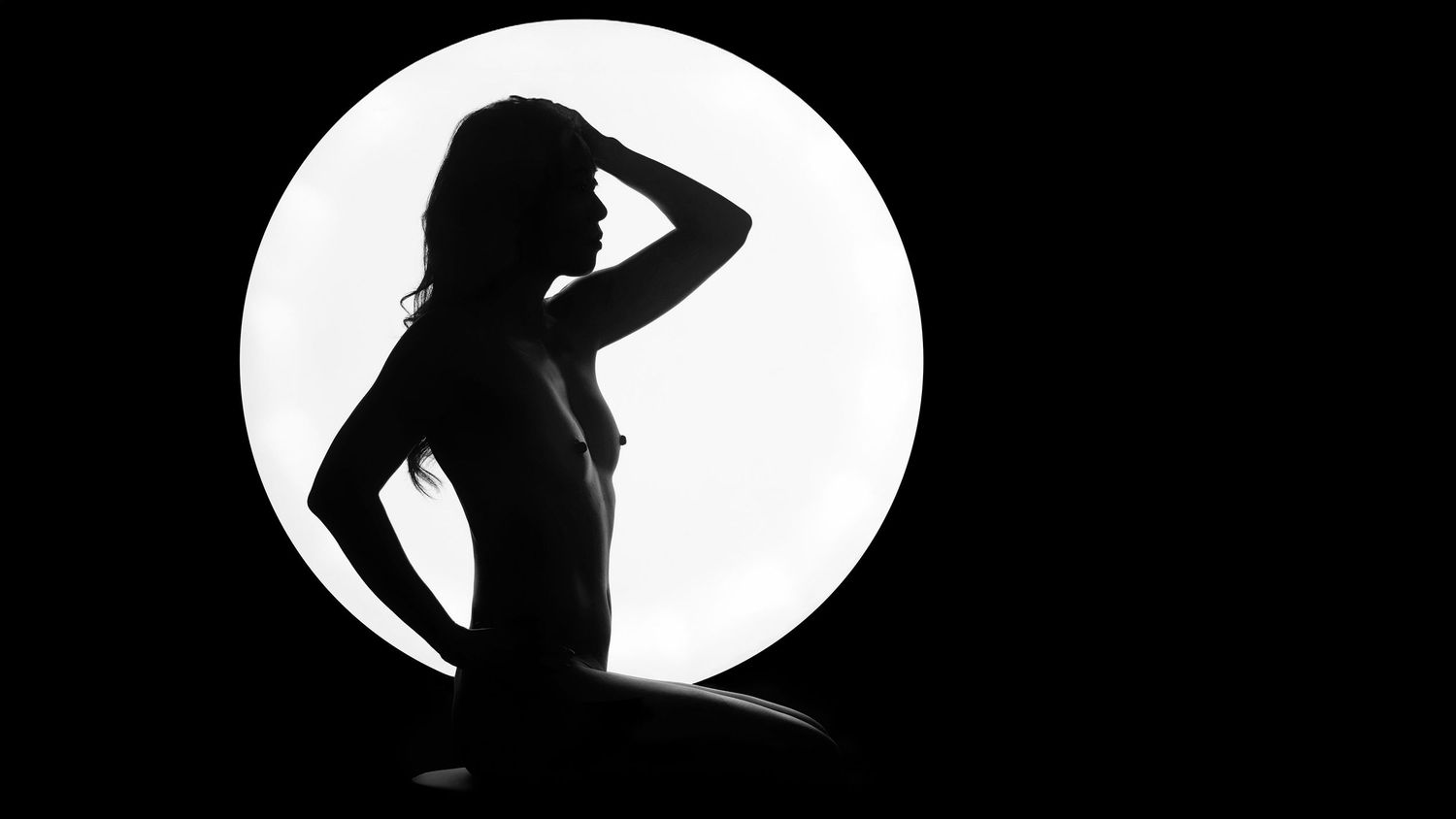Dramatic silhouetted boudoir photo against a white circular backdrop showing an elegant pose.