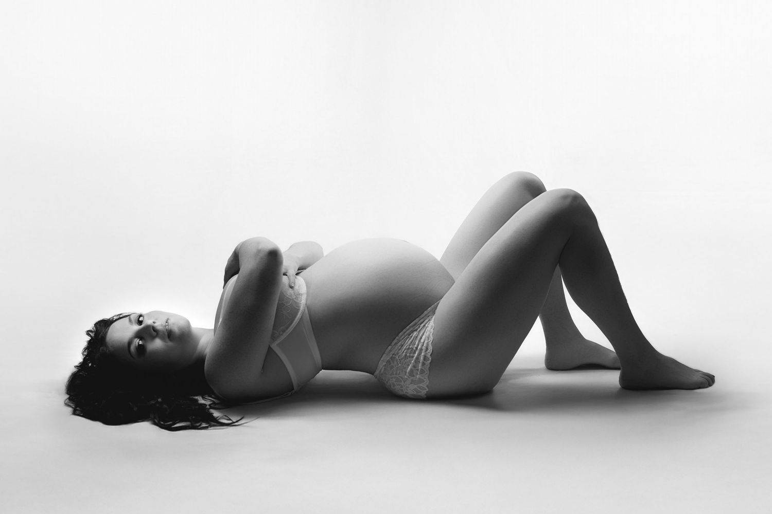 A woman posing for a maternity boudoir session against a white background.
