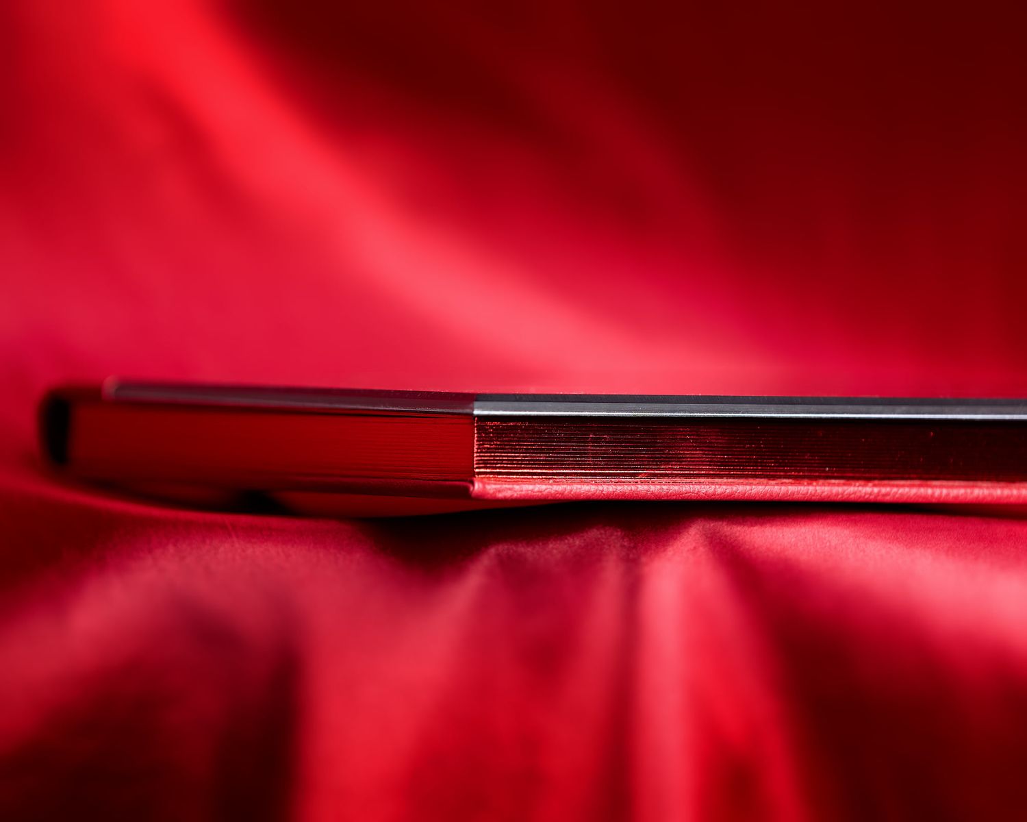 A professional boudoir album, Charlotte, sits on red silk, displaying the red binding.
