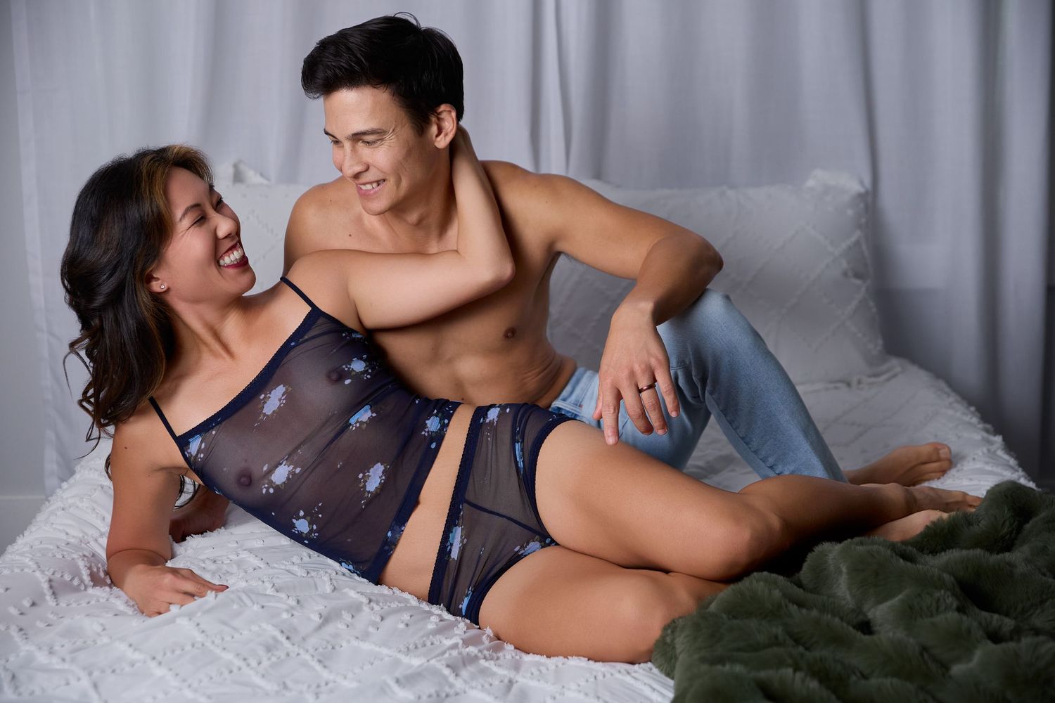 A romantic couple poses on a bed with soft lighting and muted tones for couples' boudoir photos.