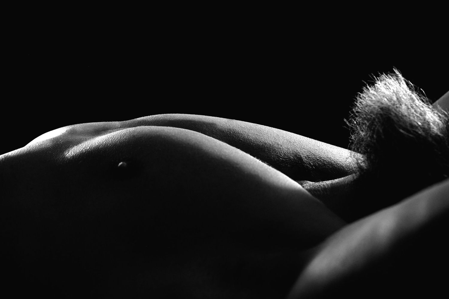 Black-and-white men's boudoir image of a male figure highlighting muscle and definition in dramatic lighting.