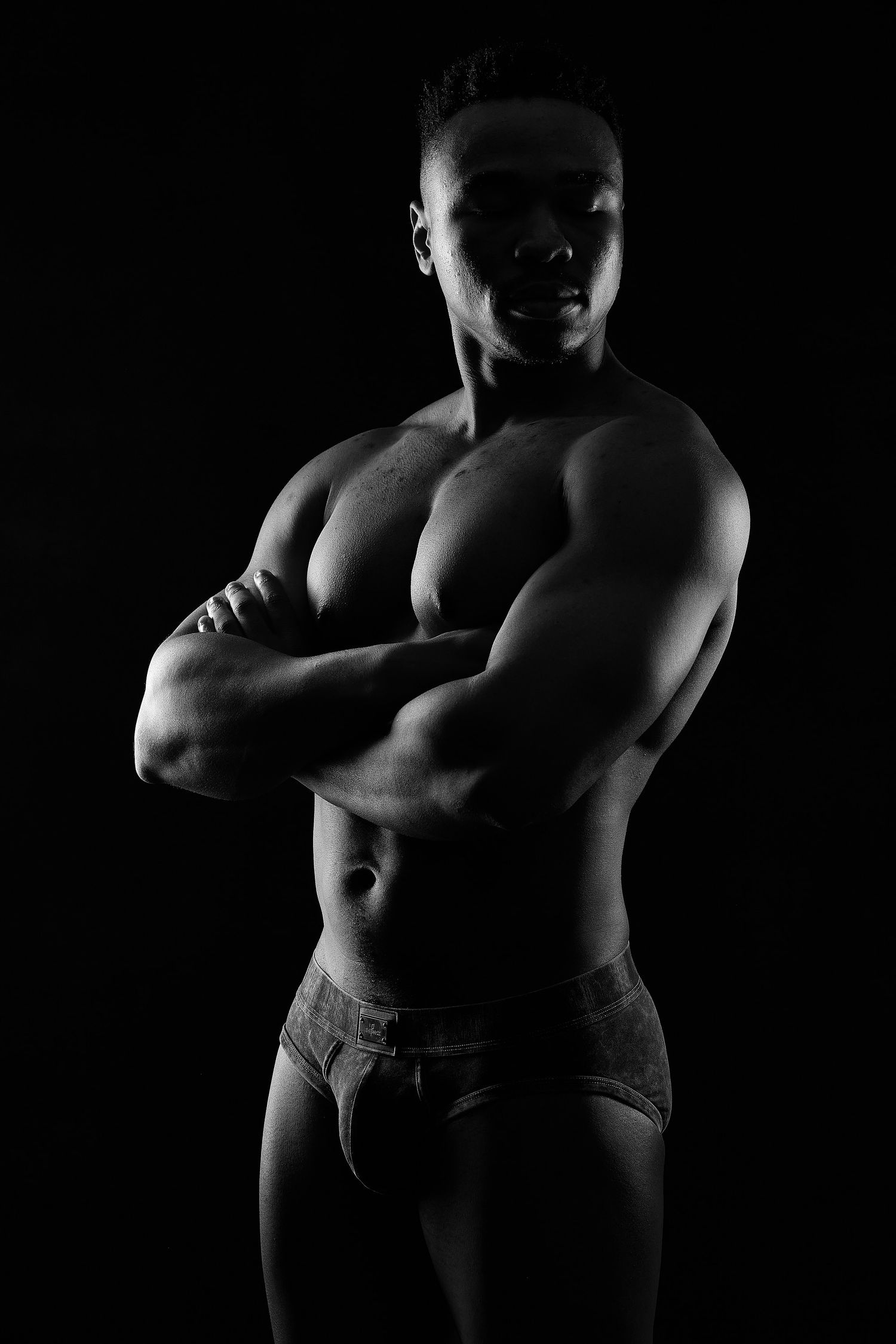 Athletic man in silhouette posing with crossed arms for a dramatic male boudoir portrait in Charlotte, NC.