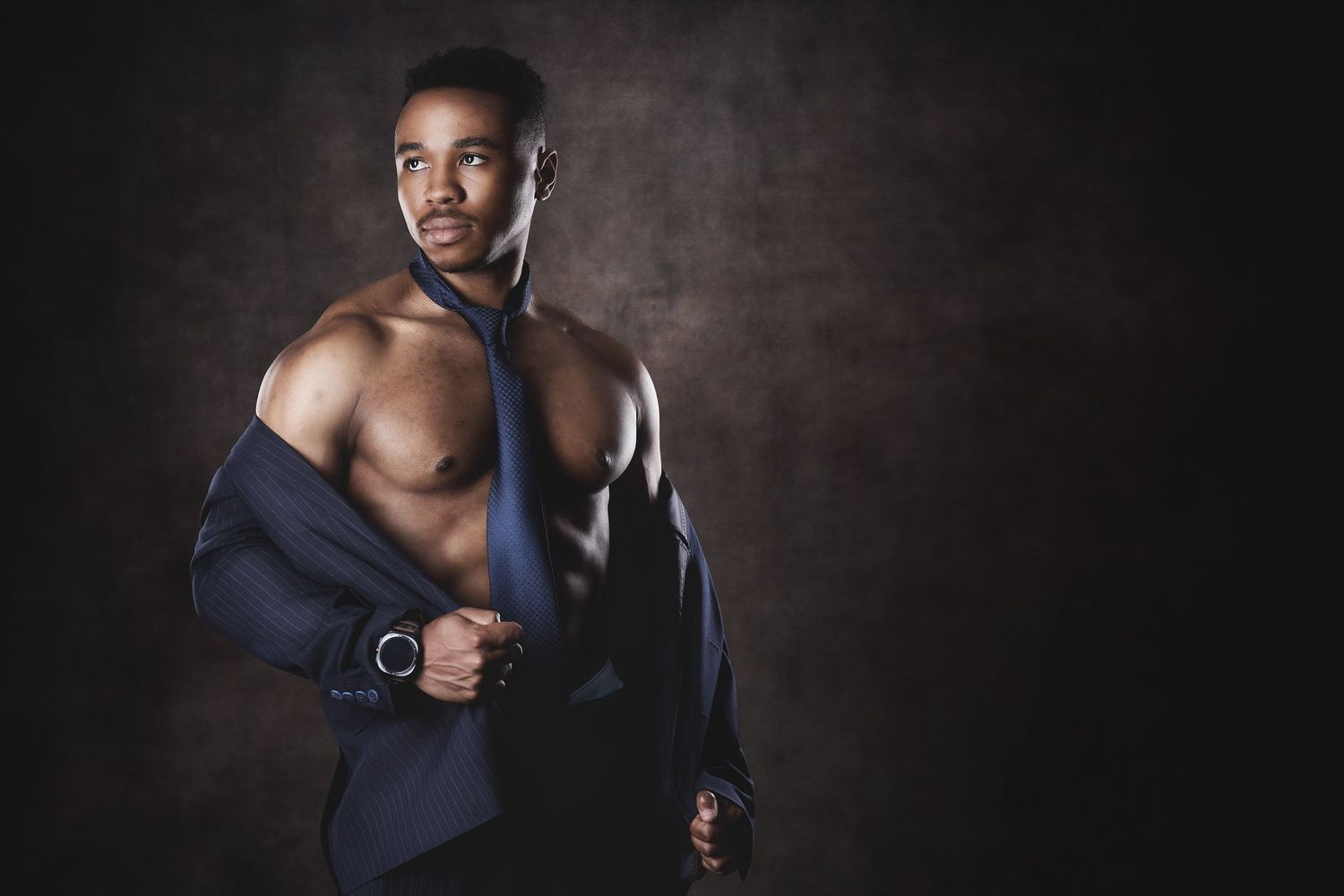 Muscular man styled with an unbuttoned shirt and necktie in a sleek male boudoir photography session in Charlotte, NC.