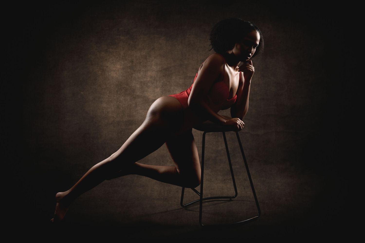 Luxury Charlotte boudoir photography of a woman leaning on a chair in the studio with guided posing and editorial lighting.