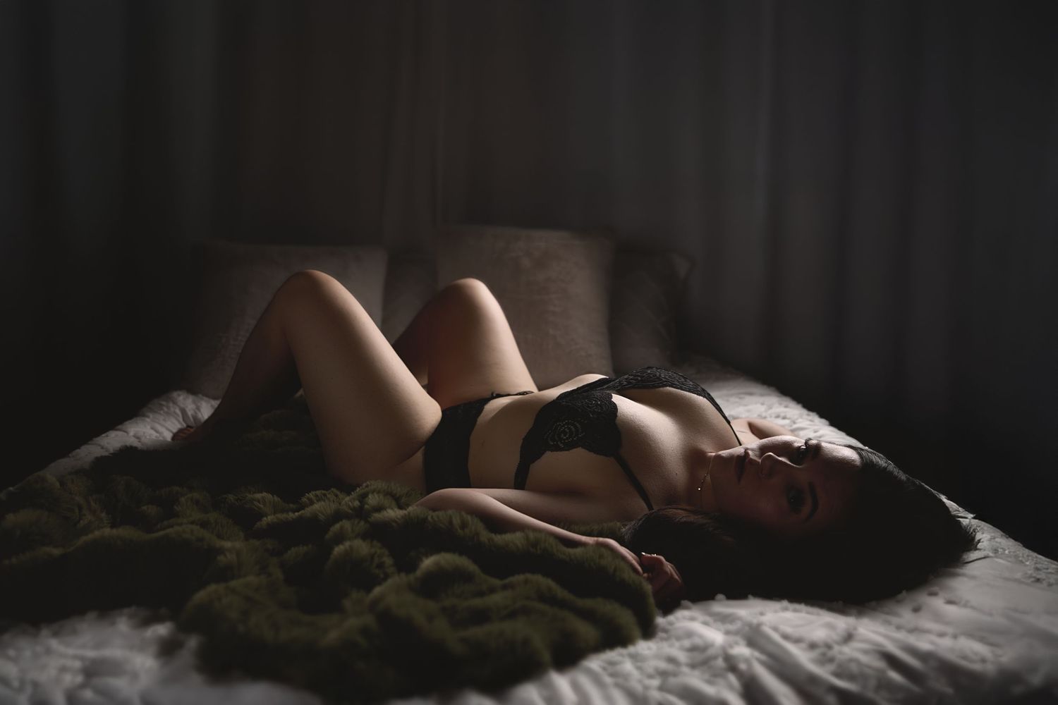 Charlotte boudoir photography of a woman posing confidently on a bed in black lingerie and cinematic lighting.