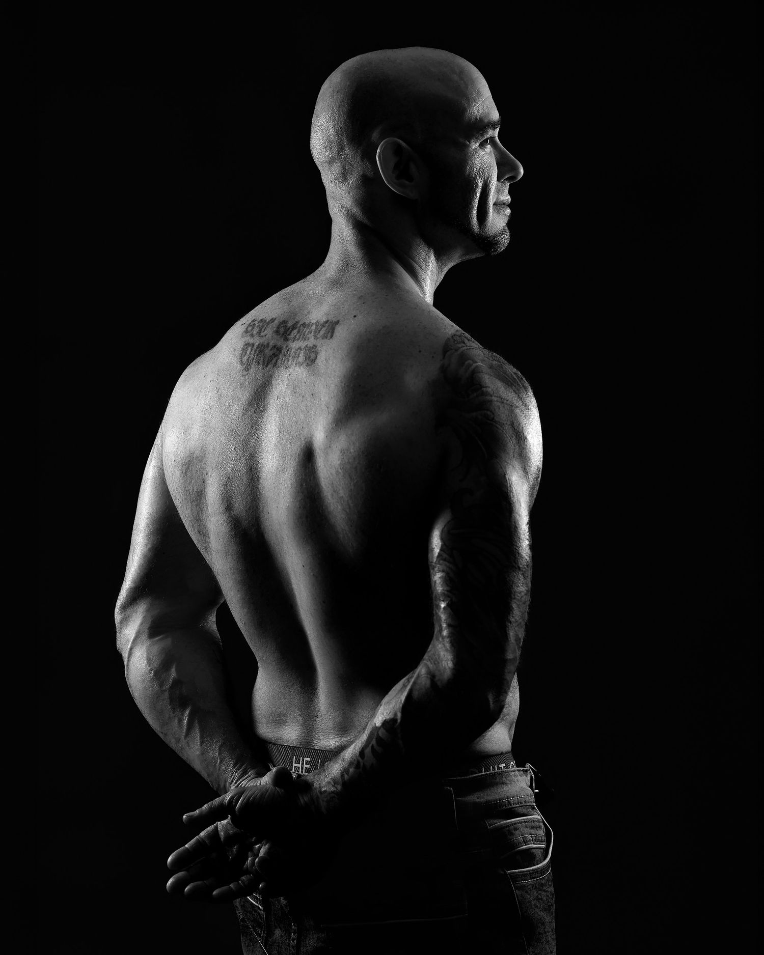 Dramatic black and white male boudoir photography in a Charlotte studio, highlighting athletic back definition and fine-art lighting.