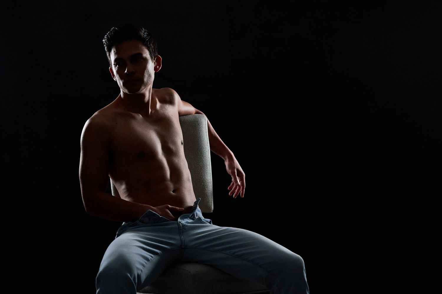 Male boudoir styling featuring dark denim and moody lighting for a rugged, masculine look.
