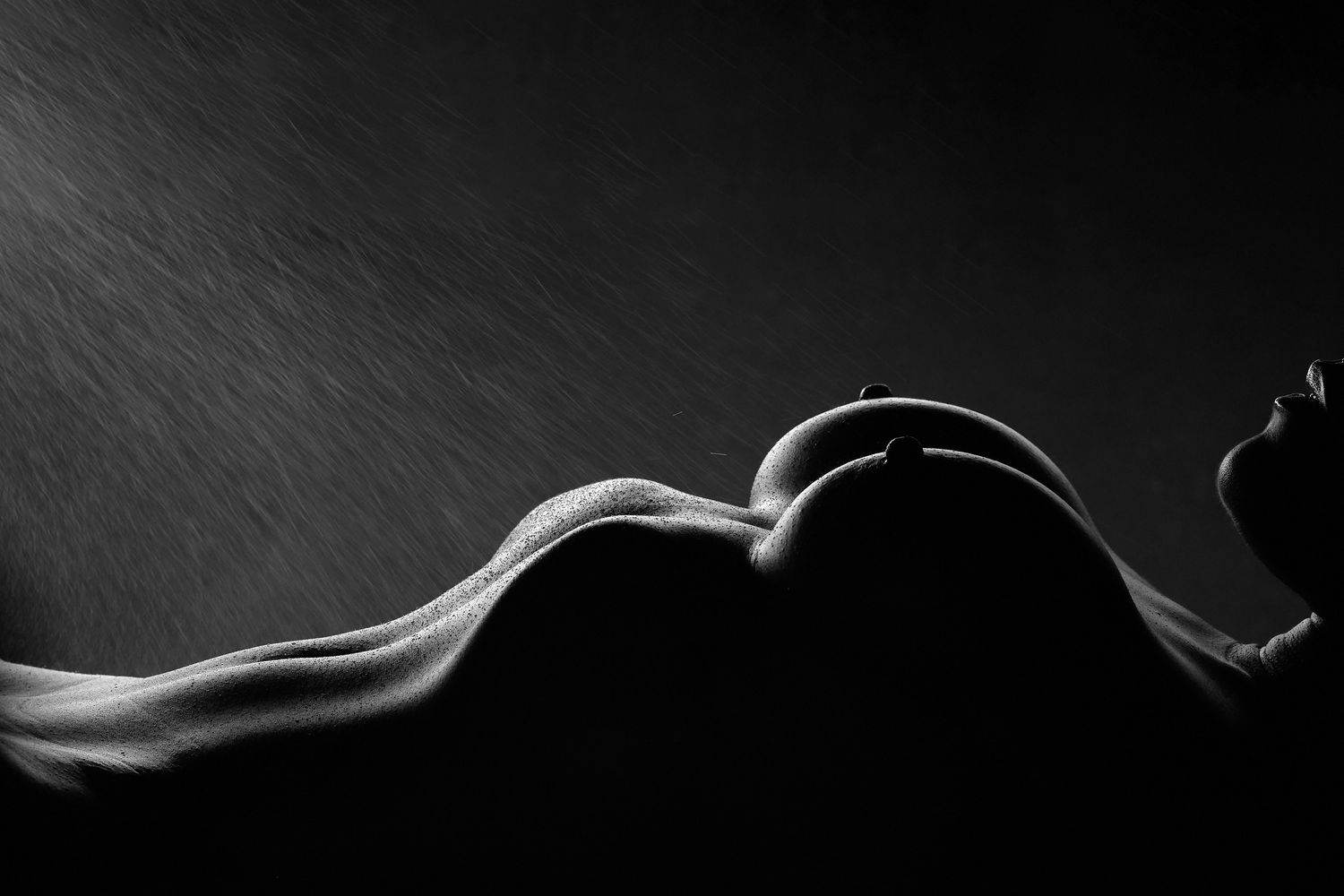 Erotic boudoir portrait in a Charlotte studio featuring a woman sprayed with water, with moody lighting.