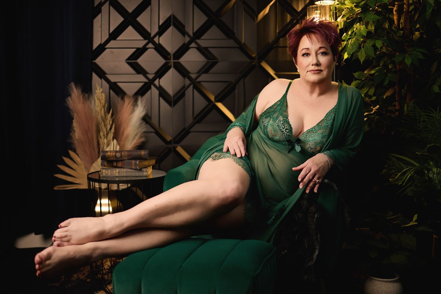 A woman in green lingerie sitting on a velvet chair, featuring professional cinematic lighting at a Charlotte boudoir studio.
