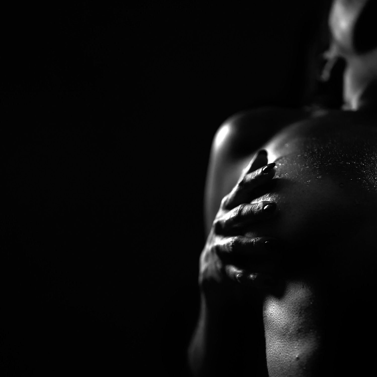 Dramatic black and white close-up of a hand resting on skin in low key lighting.