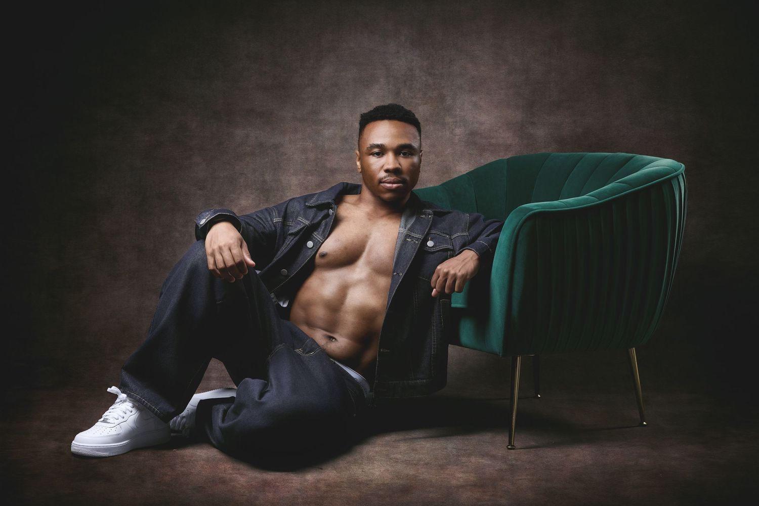 Handsome man sitting in a green velvet chair wearing an unbuttoned jacket for a luxury men's portrait session in Charlotte, NC.
