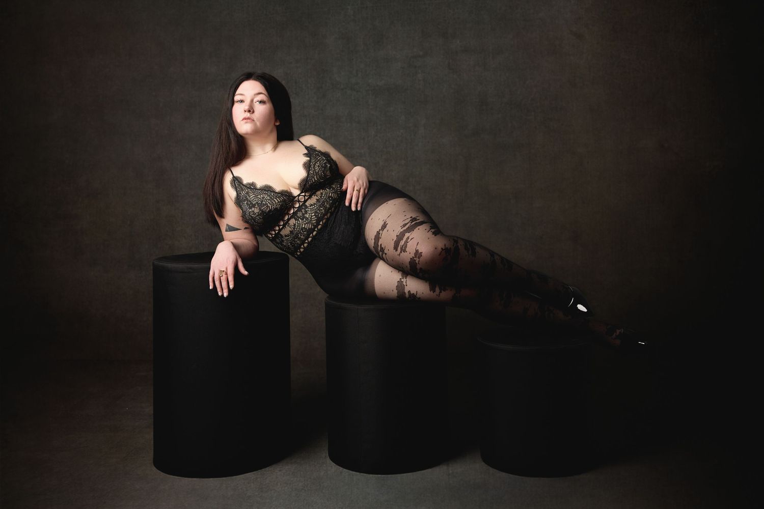 High-End boudoir experience in Charlotte, of a woman wearing black lingerie in cinematic lighting on a dark studio backdrop.