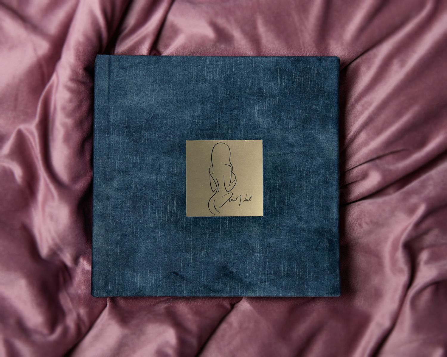 A velvet boudoir album sits elegantly on soft, pink fur, showcasing the album cover with a gold plate that says IronVeil Boudoir.