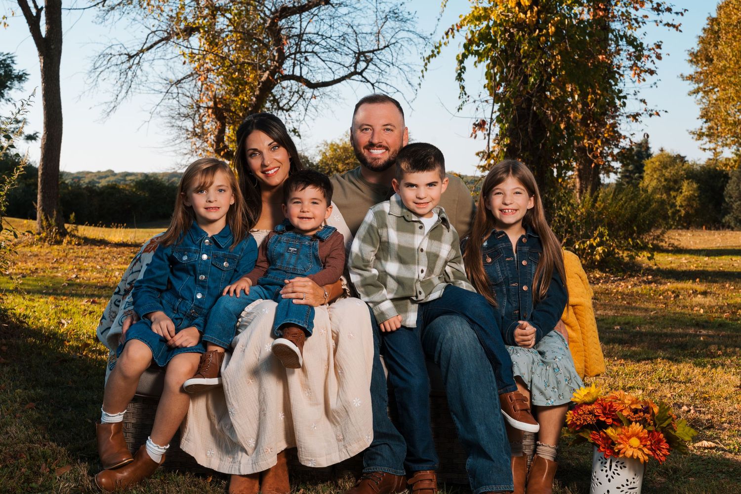 Family portrait in casual attire during golden hour with fall foliage in background.