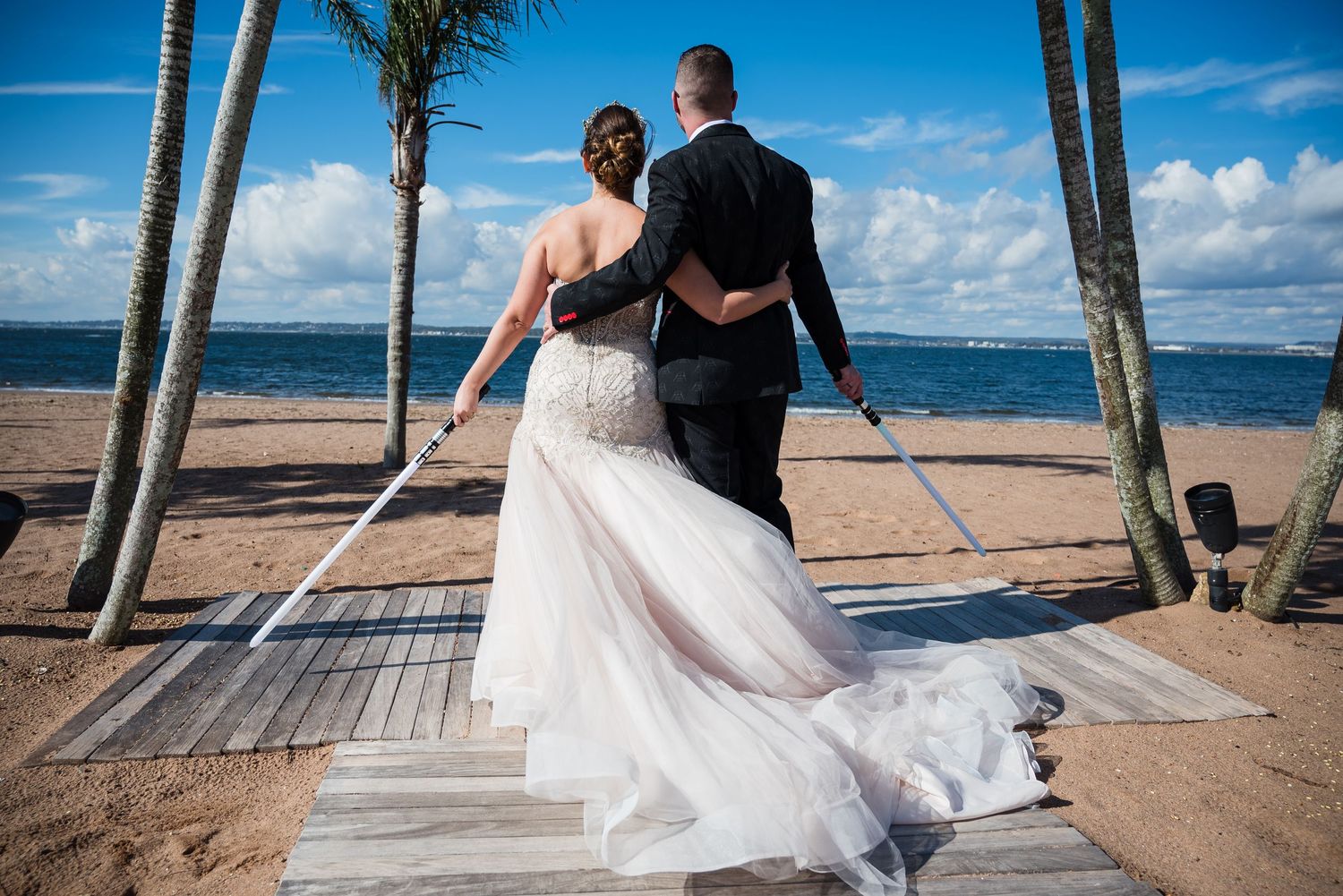 Wedding couple walking along a tropical beach boardwalk with palm trees and ocean views.