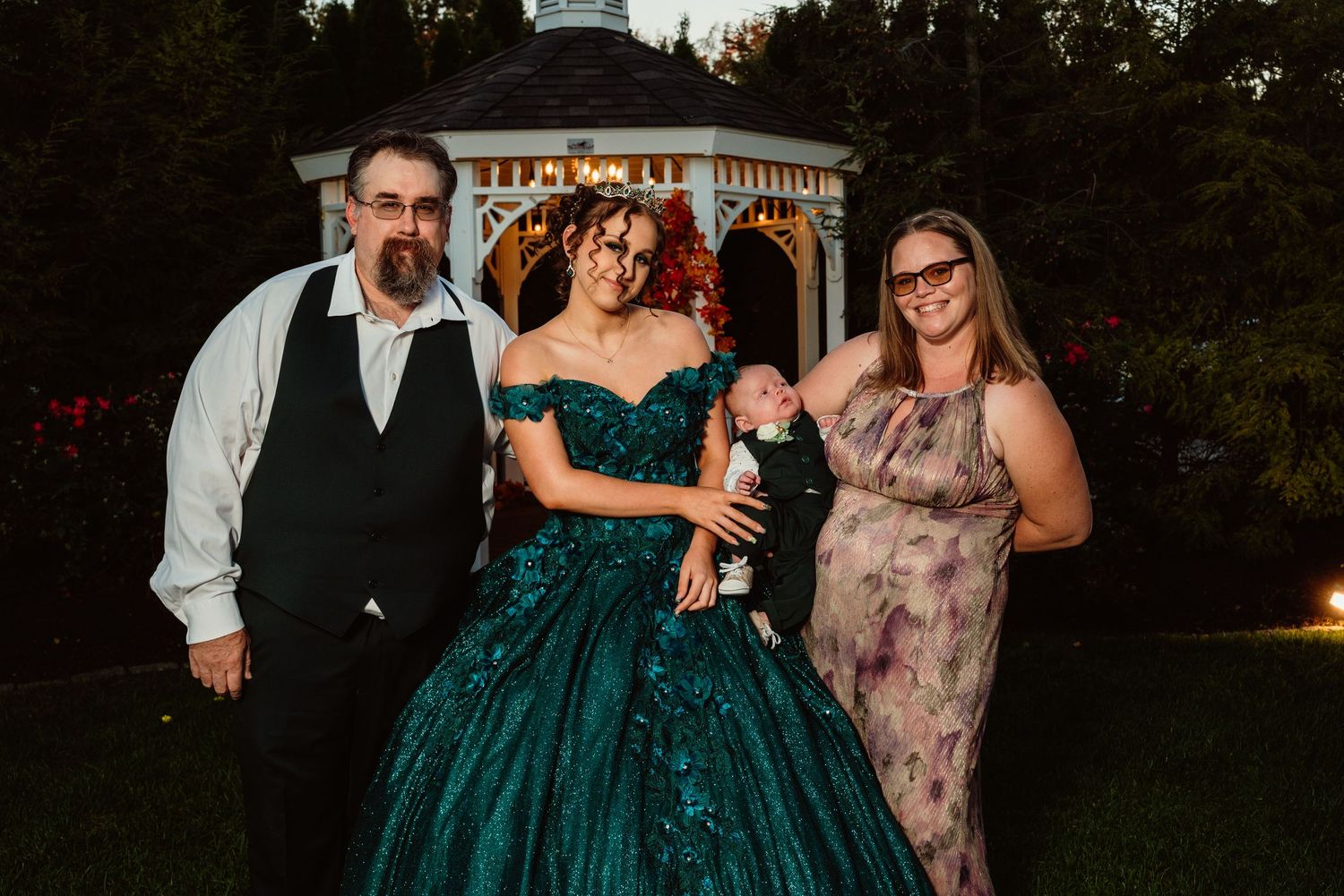 Group photo of wedding party members in formal attire at an outdoor venue.