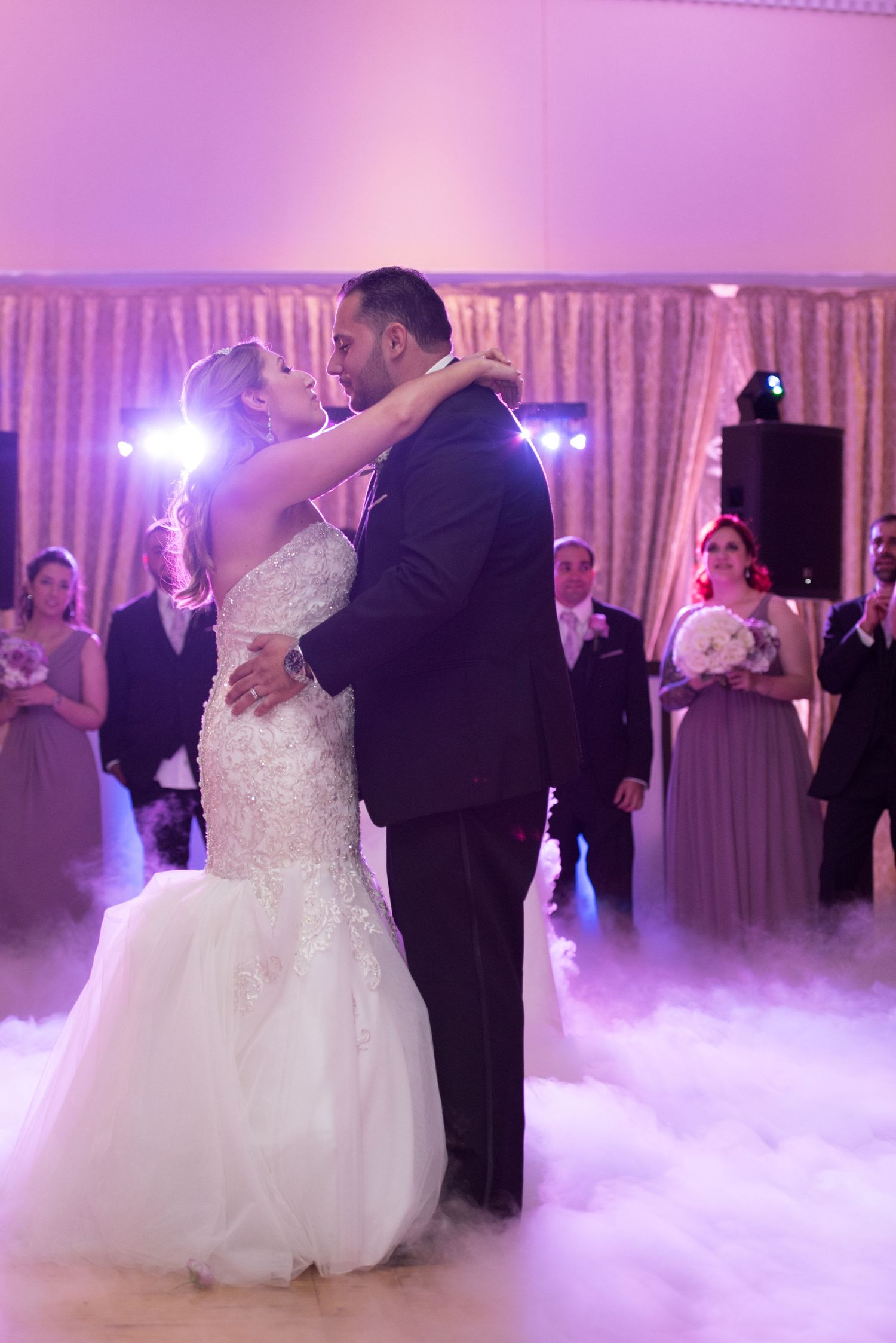 Newlyweds share their first dance surrounded by fog effects and purple lighting at their wedding reception.