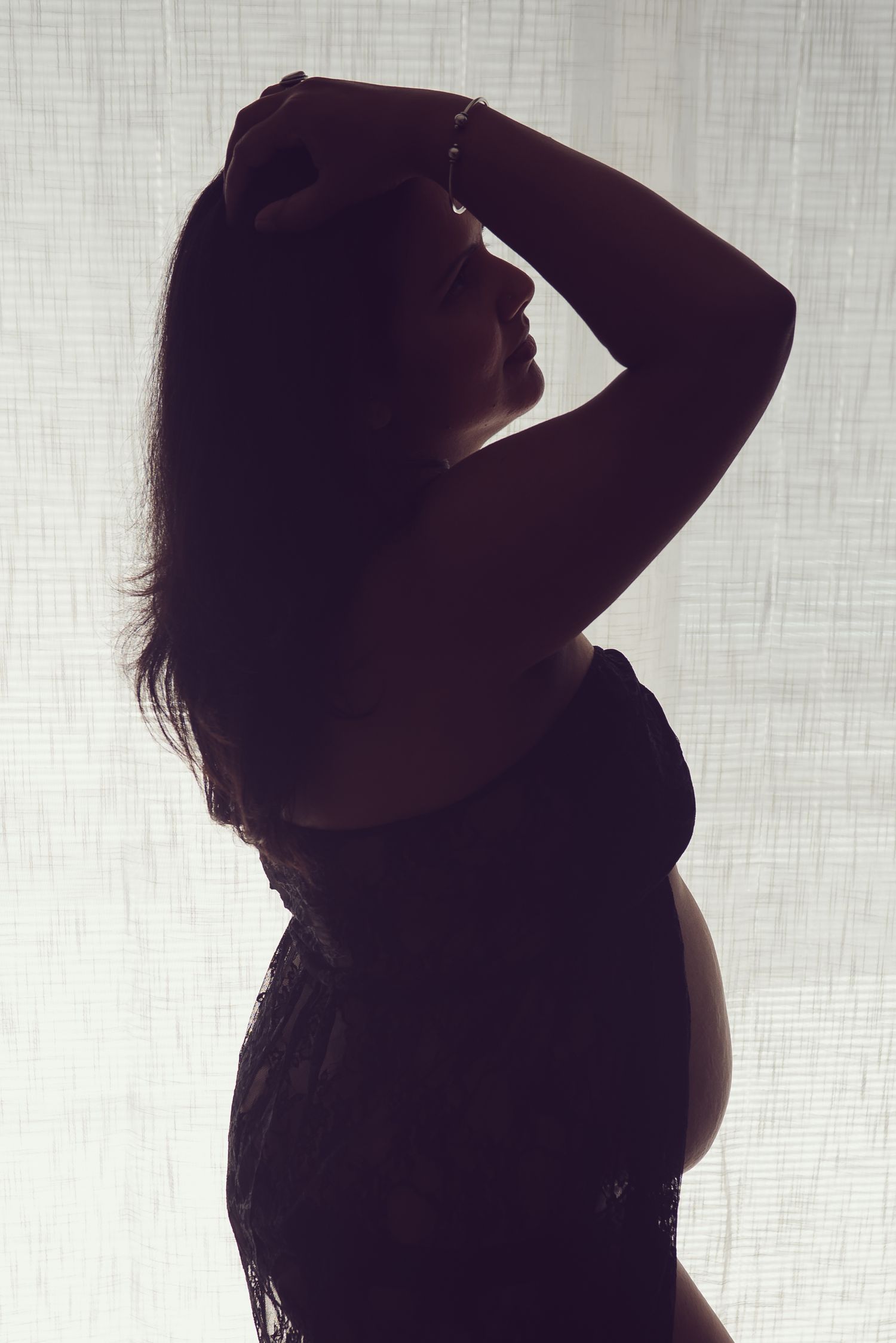 Dramatic silhouette of pregnant woman in profile against light background.