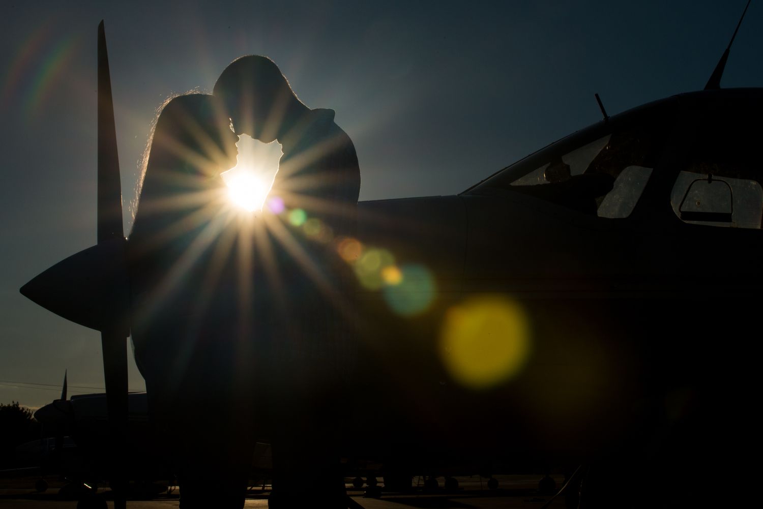 Silhouettes of aircraft against a dramatic sunset sky with lens flare effects.