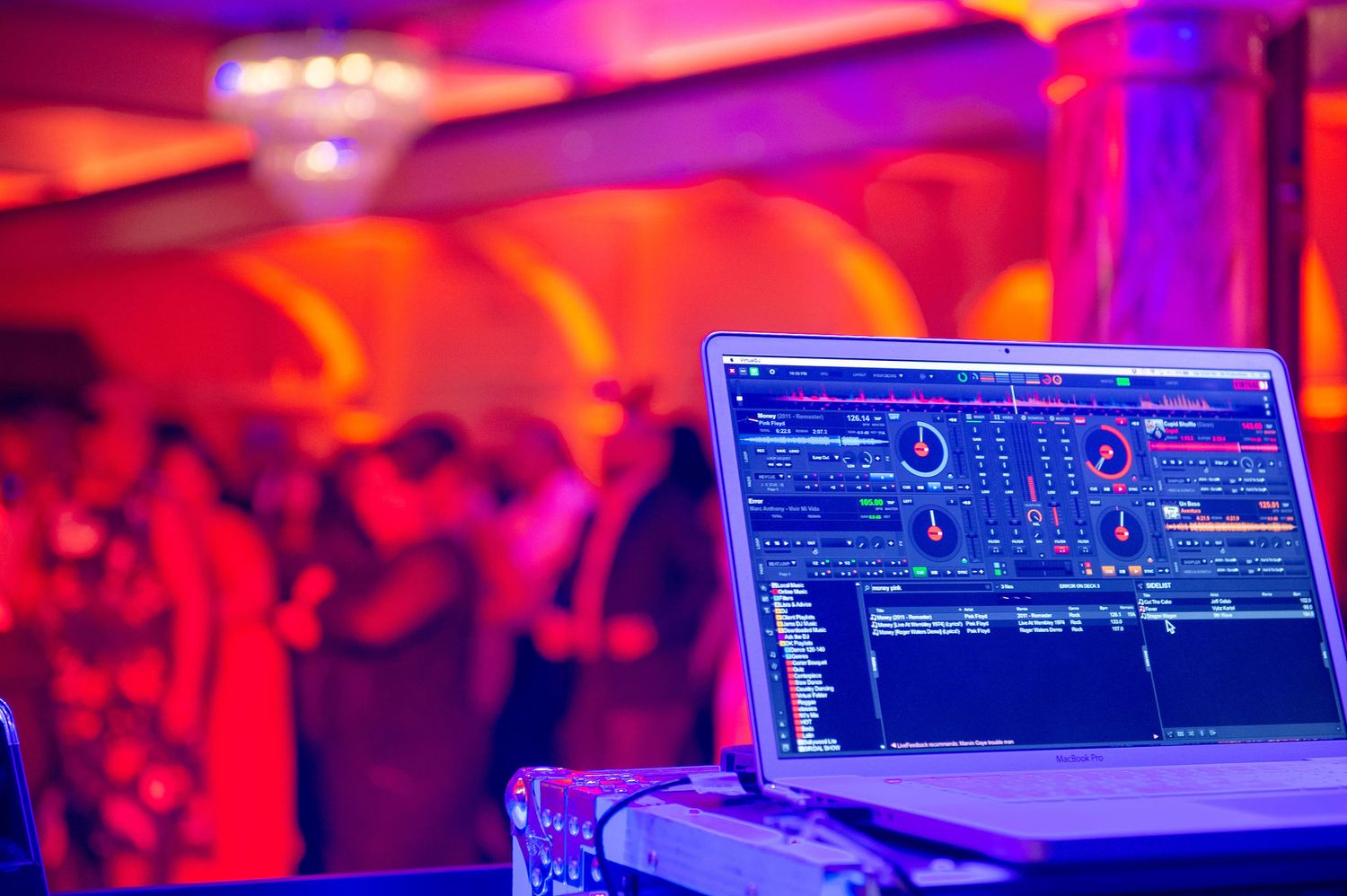DJ equipment and controllers illuminated by vibrant red and blue stage lighting.