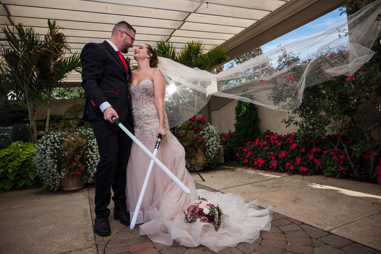 Wedding couple poses against a light colored wall with elegant floral bouquet.