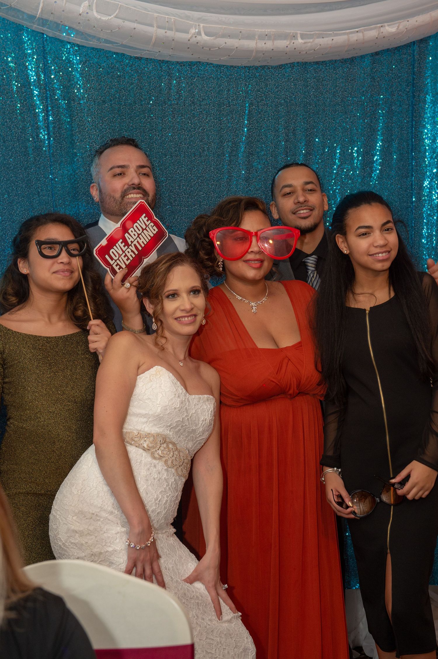 Wedding party members gather for group photos in front of a turquoise sequin backdrop.