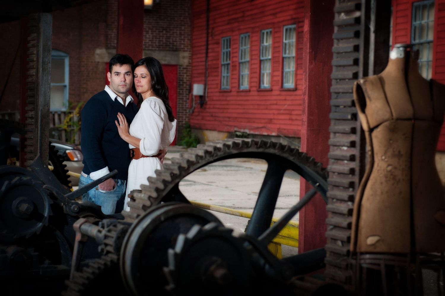 A romantic couple poses against a red brick wall in dramatic lighting creating moody engagement photos.