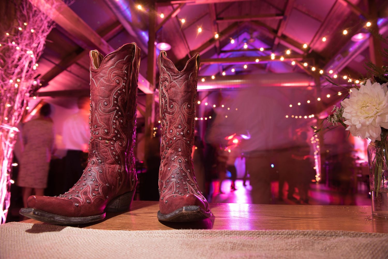 Close-up of cowboy boots on a dance floor illuminated by pink and purple party lighting.