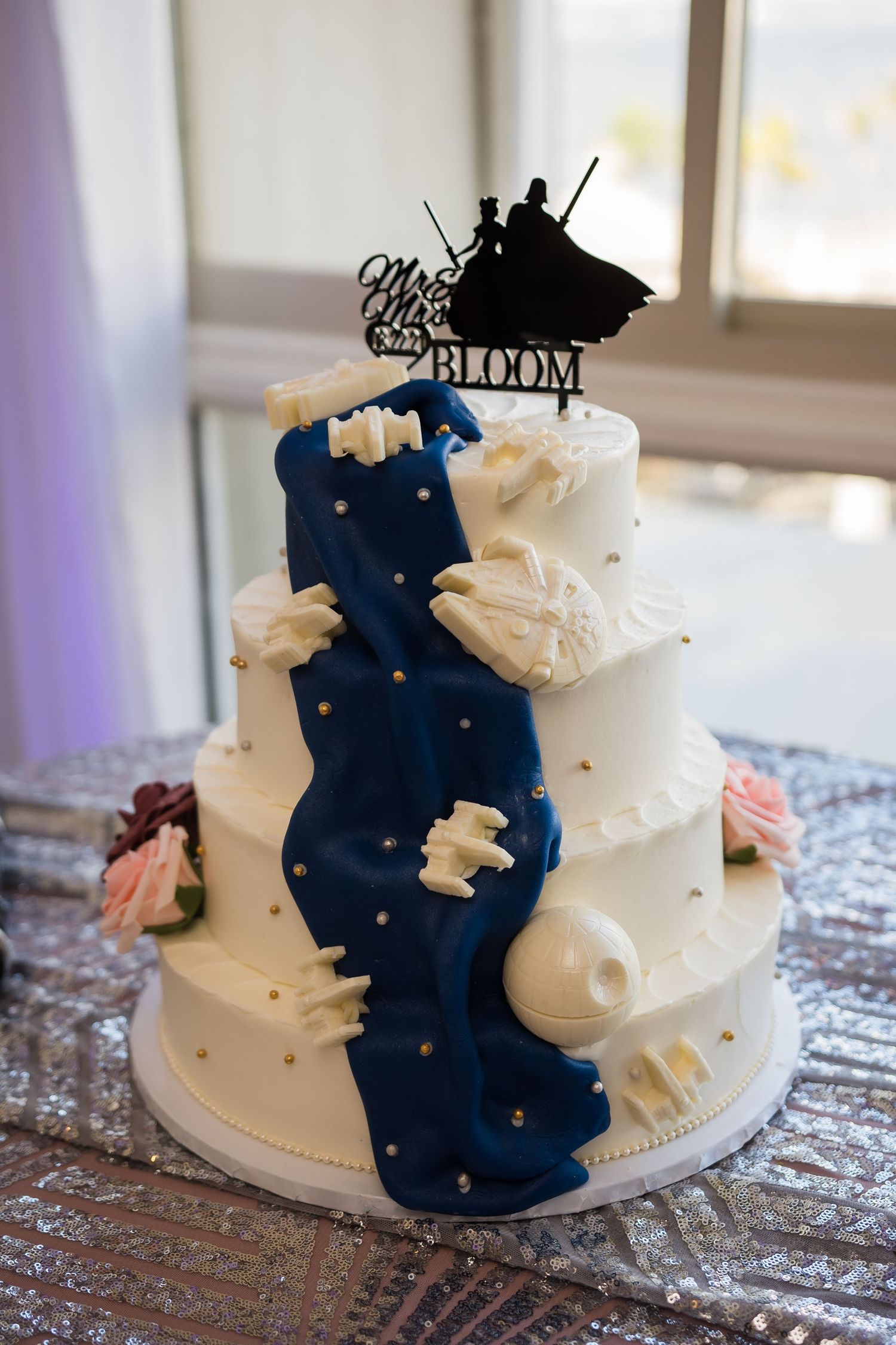 White wedding cake decorated with navy blue accents and a silhouette topper.