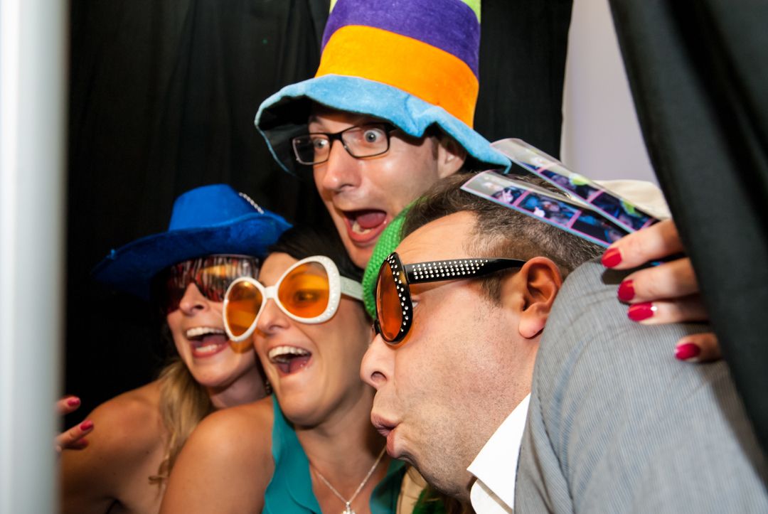 Party guests wearing colorful hats and novelty glasses posing for fun group photo.